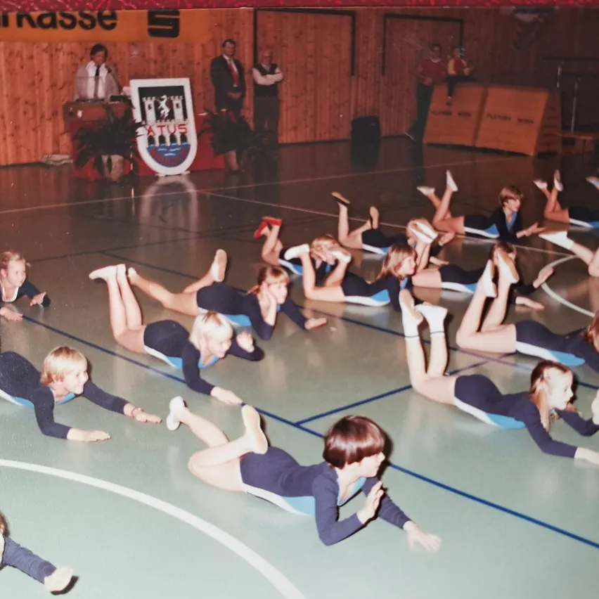 Eine Gruppe junger Frauen führt Gymnastik auf einem Platz aus, in passenden Uniformen.
