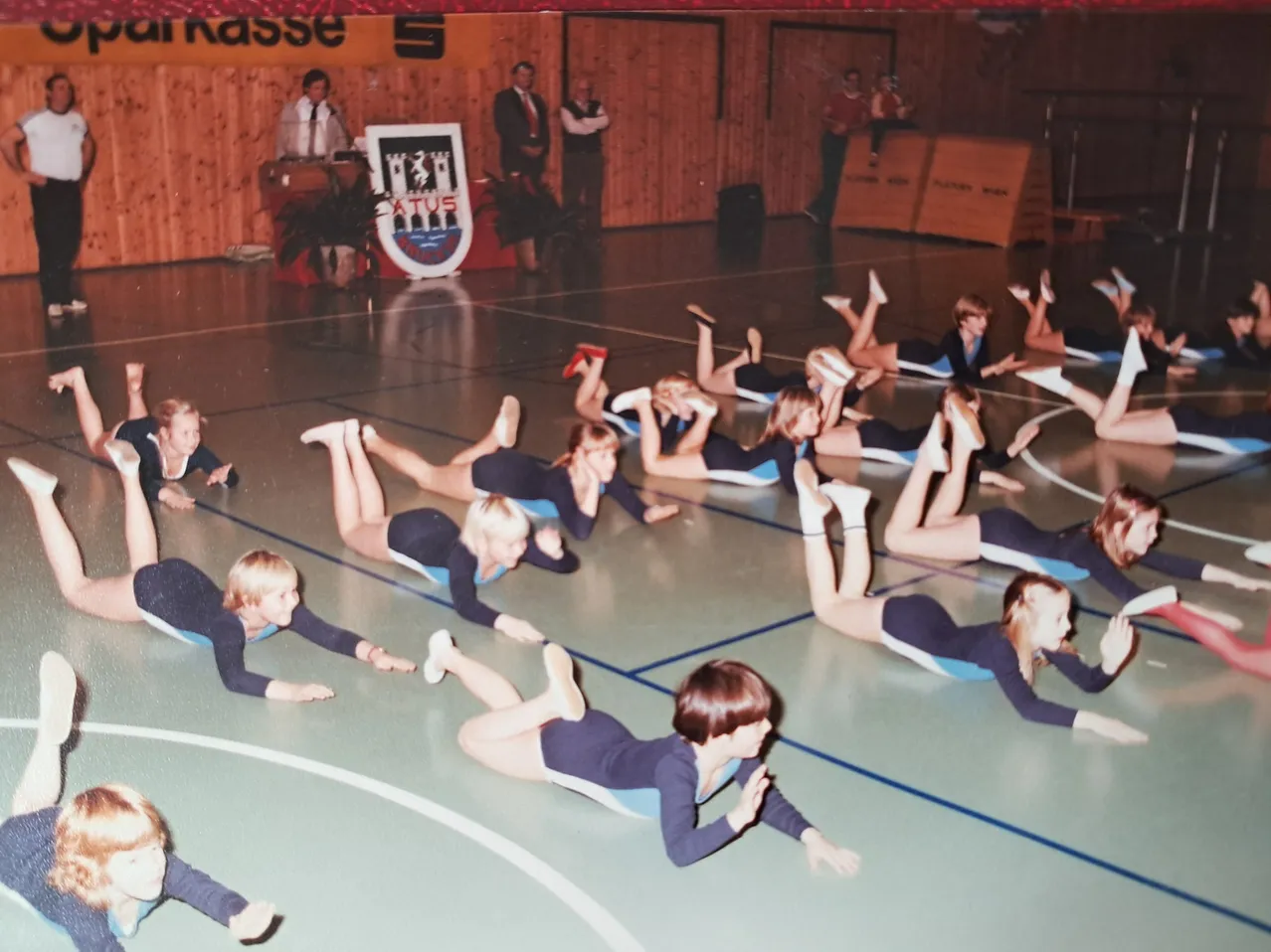 Eine Gruppe junger Frauen führt Gymnastik auf einem Platz aus, in passenden Uniformen.