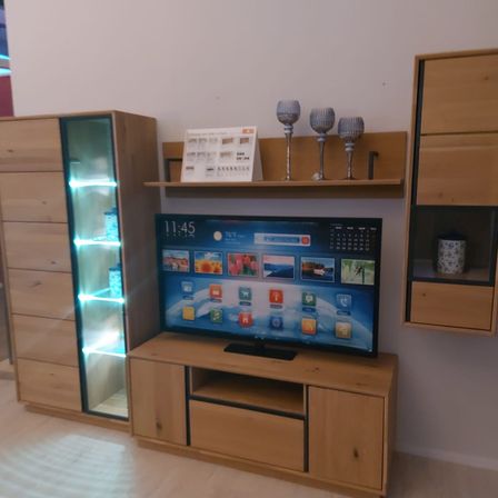 Ein Wohnzimmer mit einem hölzernen Entertainment-Center, einem Flachbildfernseher und Regalen mit Weingläsern und einem Kalender.