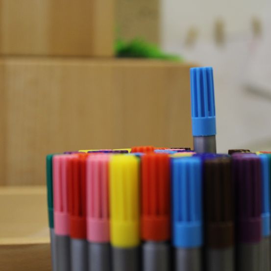 Eine Nahaufnahme einer Sammlung farbiger Marker, hauptsächlich in Rot-, Gelb-, Blau- und Grüntönen, wobei ein Marker seinen Deckel aufgesetzt hat.