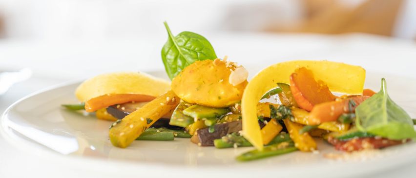 A plate of fresh vegetables, including carrots, zucchini, and green beans, garnished with basil leaves and sesame seeds.