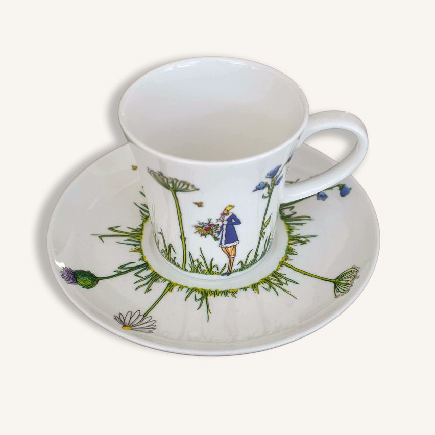Eine weiße Porzellantasse und Untertasse mit Blumendesigns, die eine Person in einem blauen Mantel und gelber Hose zeigt.