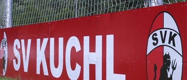 Ein roter Banner mit weißem Text zeigt 'SV KUCHL' und ein Logo eines Teufels mit einer Heugabel auf der rechten Seite. Hinter dem Banner befindet sich ein Fußballtor mit Netz.