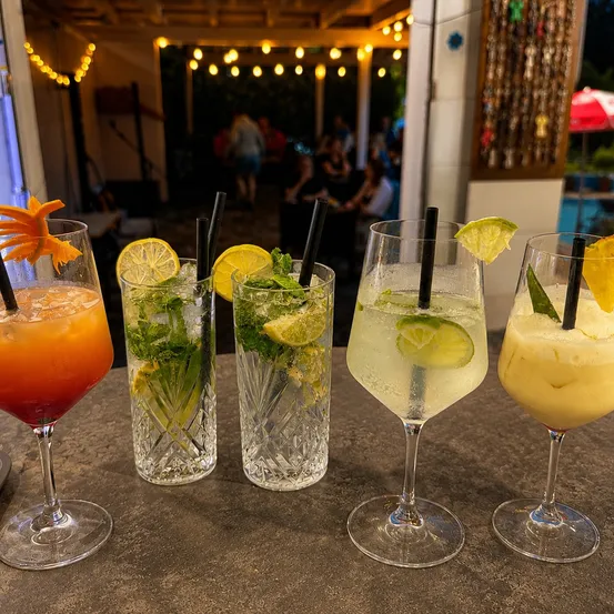 Fünf Gläser Cocktails mit Garnierungen auf einem Tisch, einschließlich eines Glases mit Zitronenscheibe und Minzblättern.