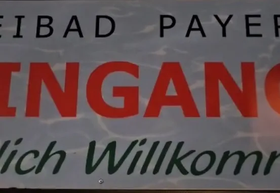 Ein Schild auf Deutsch mit dem Text 'Reibad Payerb Eingang Herzlich Willkommen' und einem Wasserhintergrund.