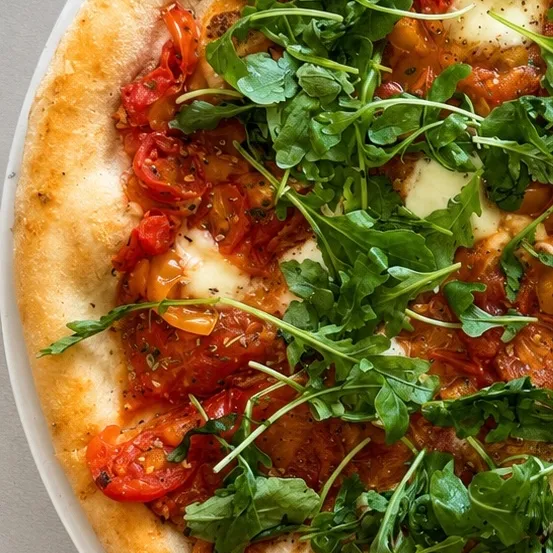 Eine Nahaufnahme einer Pizza mit Kirschtomaten, Mozzarella und Rucola auf einem weißen Teller.