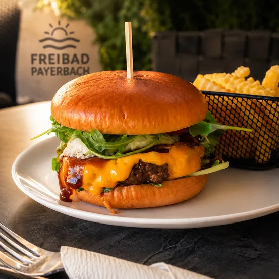 Ein Cheeseburger mit geschmolzenem Käse, Rucola und einem Zahnstocher auf einem weißen Teller mit einer Beilage Pommes frites.