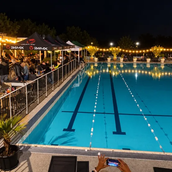 Eine nächtliche Veranstaltung an einem Außenpool mit Gästen, die rund um den Pool essen, beleuchtet durch Lampen und Zelte.
