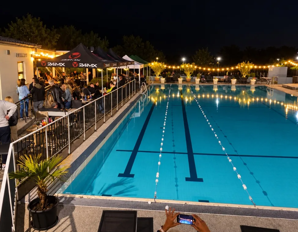 Eine nächtliche Veranstaltung an einem Außenpool mit Gästen, die rund um den Pool essen, beleuchtet durch Lampen und Zelte.