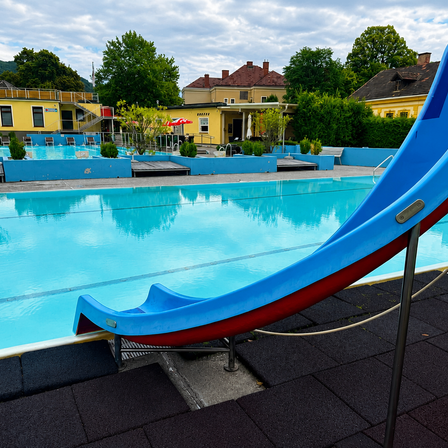 Ein Freibad mit einer blauen Rutsche und einem gelben Gebäude im Hintergrund.