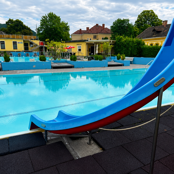 Ein Freibad mit einer blauen Rutsche und einem gelben Gebäude im Hintergrund.