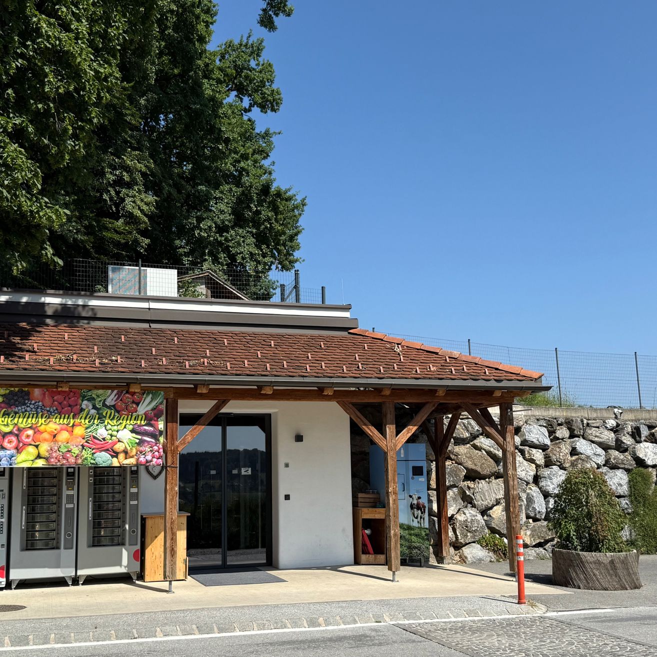 Ein Laden mit braunem Dach und einem Schild, das lokale Produkte anbietet. Der Laden hat Glastüren und eine kleine Veranda. Zwei Schließfächer zum Aufbewahren von Gegenständen befinden sich auf der linken Seite.