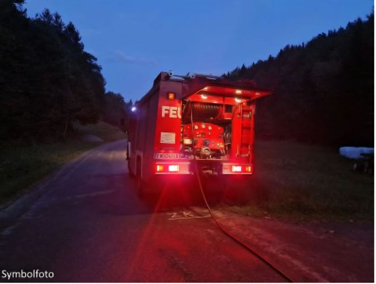 Ein roter Feuerwehrwagen steht bei Nacht am Straßenrand, mit eingeschalteten Blaulicht, möglicherweise im Einsatz.
