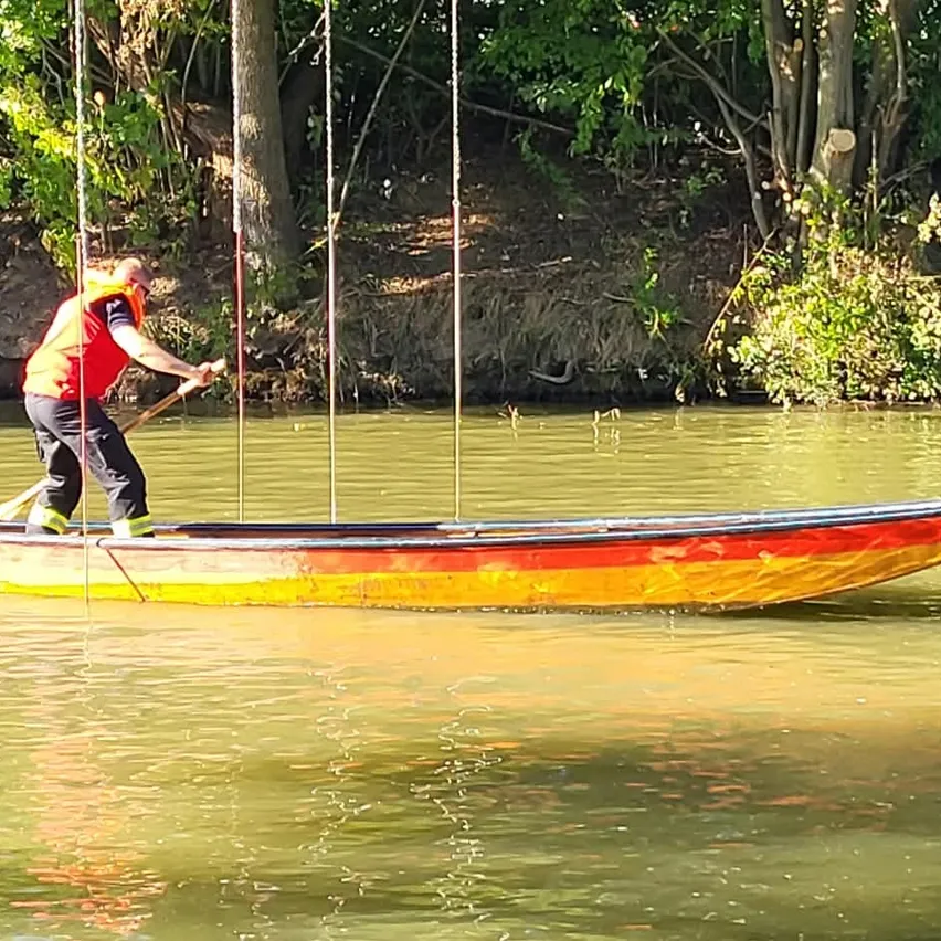 Ein Mann in einem roten Rettungsweste paddelt ein Boot auf einem Fluss mit klarem Himmel oben.