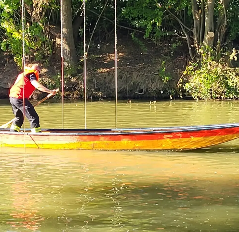 Ein Mann in einem roten Rettungsweste paddelt ein Boot auf einem Fluss mit klarem Himmel oben.