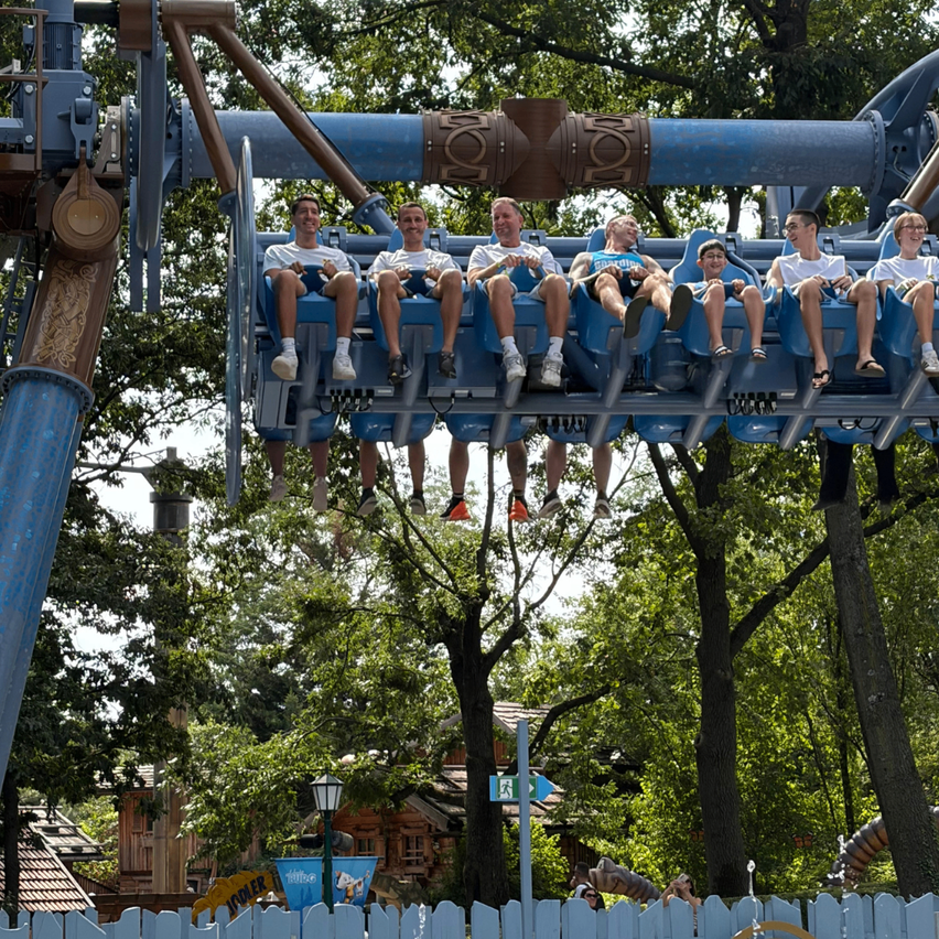 Eine Gruppe von Menschen sitzt auf einer blauen Achterbahn in einem Vergnügungspark.