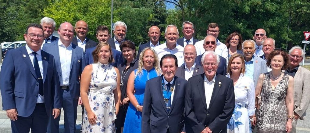 Eine Gruppe von formell gekleideten Menschen steht auf einer Steintreppe und lächelt für ein Foto. Der Mann in der Mitte trägt eine Medaille, während andere Krawatten und Brillen tragen.