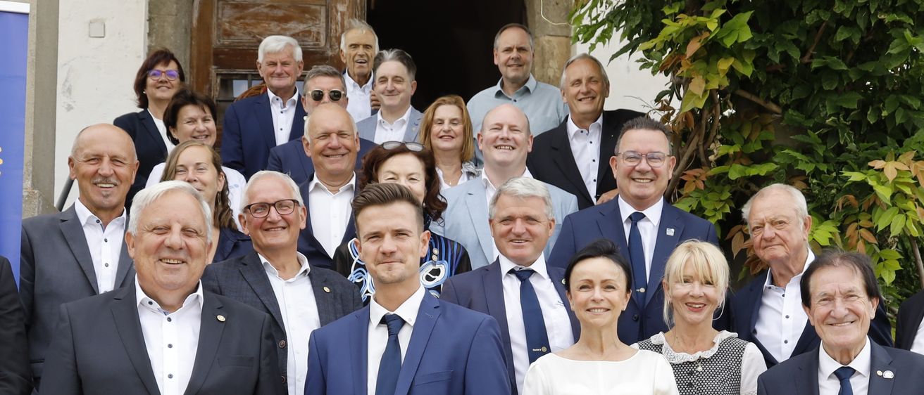 Eine Gruppe von Menschen, darunter Männer und Frauen, posiert für ein Foto auf einer Treppe. Einige sind in formeller Kleidung, andere in lässiger Kleidung gekleidet. Ein Hund steht in der Mitte.