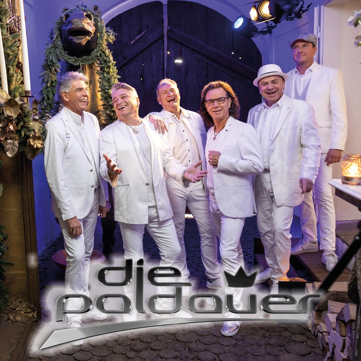 Eine Gruppe von Männern in weißen Anzügen und Hüten posiert für ein Foto vor einem geschmückten Torbogen. Dahinter steht eine große Statue und zwei Scheinwerfer.