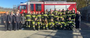 Eine Gruppe Feuerwehrleute in Uniform posiert für ein Foto vor einem roten Feuerwehrauto.