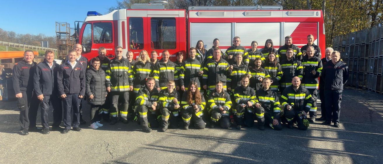 Eine Gruppe Feuerwehrleute in Uniform posiert für ein Foto vor einem roten Feuerwehrauto.