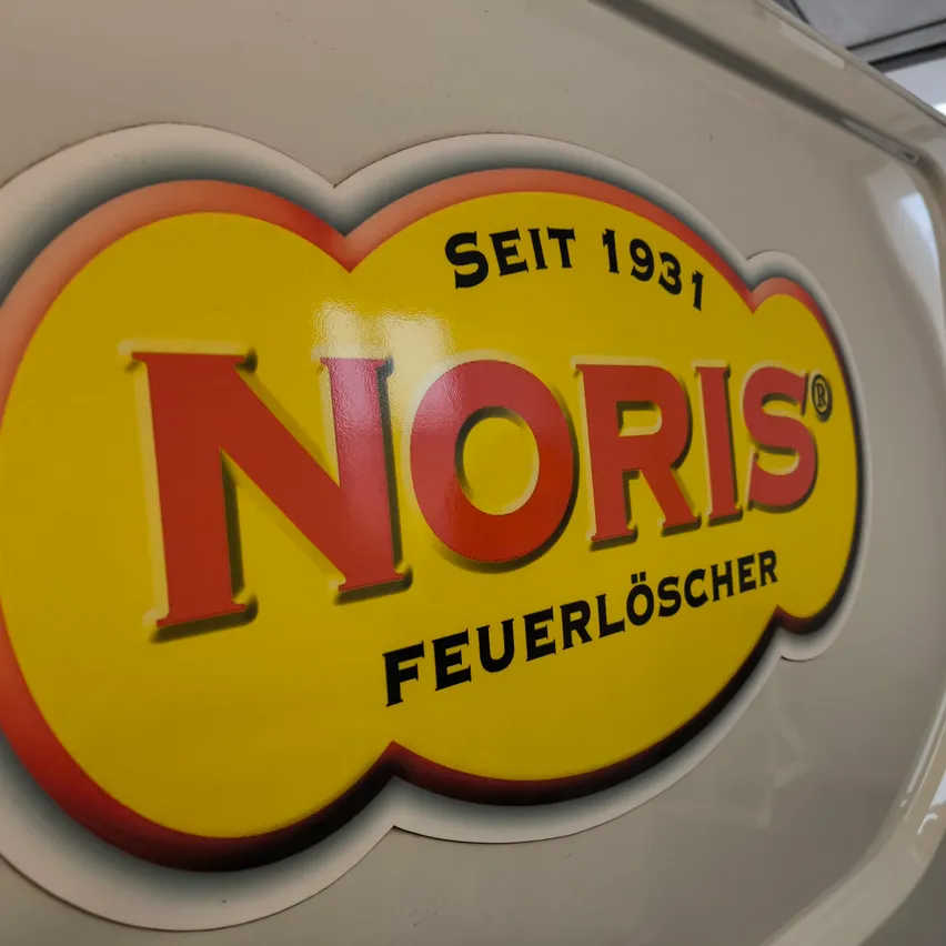 Das Norris Feuerlöscher-Logo, gegründet 1931, wird auf weißem Hintergrund gezeigt. Das Logo ist gelb mit roten und orangefarbenen Umrissen.