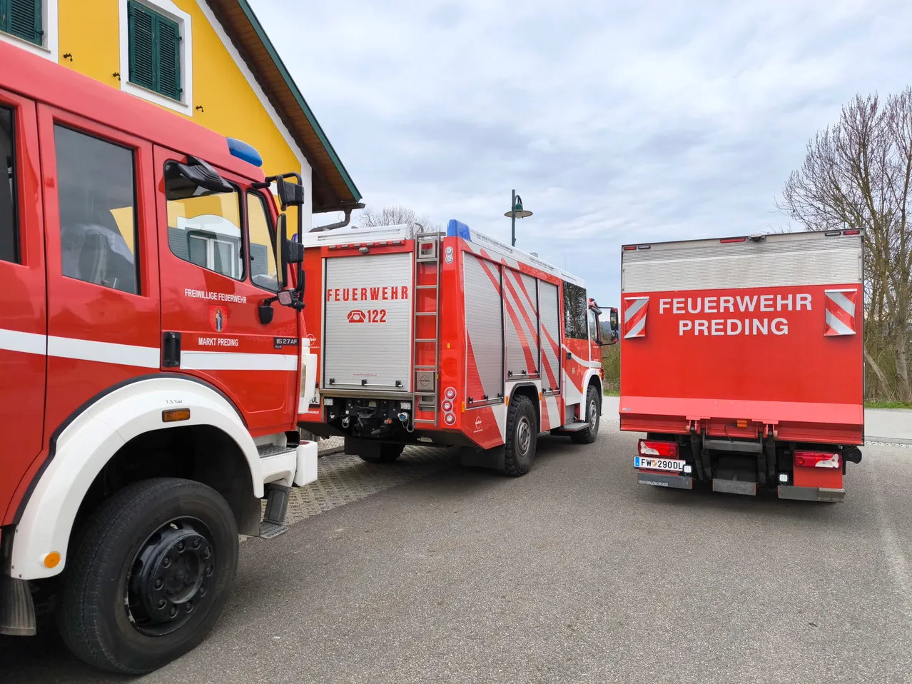 Drei rote Feuerwehrwagen sind vor einem gelben Gebäude mit einem bewölkten Himmel geparkt. Der mittlere Wagen hat die Nummer 122.