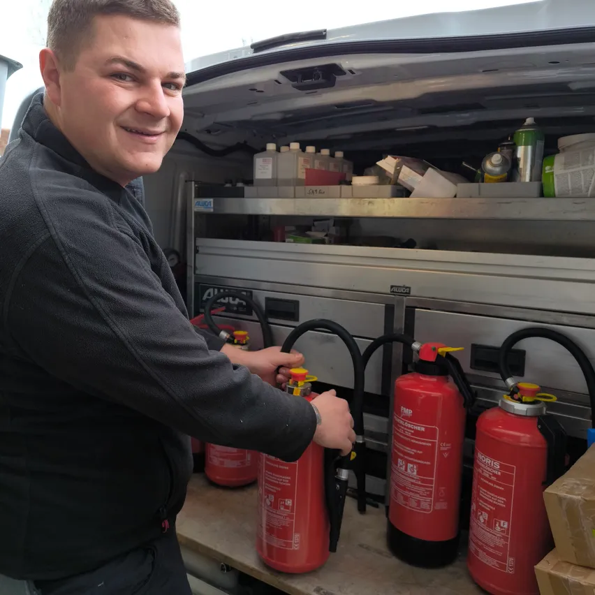 Ein Mann steht in der Nähe der Rückseite eines Fahrzeugs mit Feuerlöschern im Inneren. Er lächelt und scheint einen der Feuerlöscher zu handhaben.