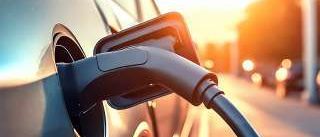 Ein schwarzer Elektrowagen wird auf einer Straße bei Sonnenuntergang geladen, wobei ein Ladekabel in seinen Ladeanschluss eingesteckt ist.