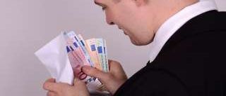Ein Mann in einem schwarzen Anzug hält einen weißen Umschlag mit 20-Euro-Scheinen in den Händen und betrachtet die Scheine.