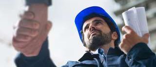 Ein Mann in einem blauen Schutzhelm schüttelt die Hand einer anderen Person und hält eine Mappe.