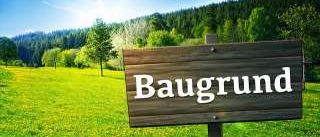 Ein Holzschild mit dem Wort 'Baugrund' steht in einem üppigen grünen Feld mit Bergen im Hintergrund.