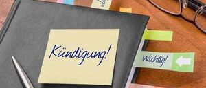 Ein Notizbuch mit Haftnotizen, die 'Kundigung!' und 'Wann?' sagen, liegt auf einem Schreibtisch mit einem Stift und einer Brille.