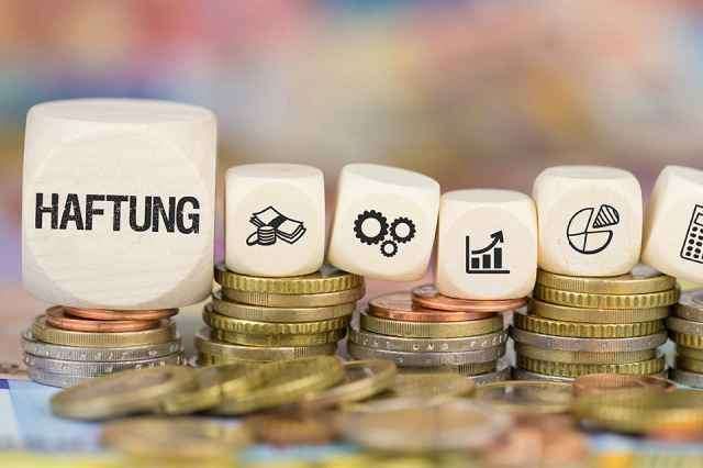 Ein Stapel Münzen mit einem Würfel, der 'Haftung' beschriftet ist, oben drauf, jeder Würfel hat ein anderes Symbol darauf.