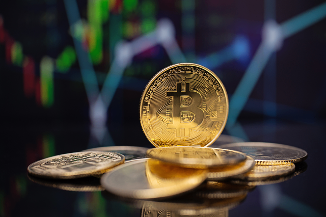 Goldene Bitcoin-Münzen werden auf einer schwarzen Oberfläche mit einem unscharfen Finanzdiagramm im Hintergrund angezeigt.