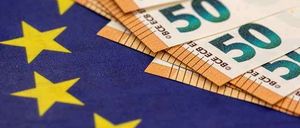 A stack of 50 euro bills on top of the European Union flag with yellow stars.