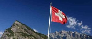 Eine Schweizer Flagge weht im Wind vor einem Hintergrund majestätischer Berge.
