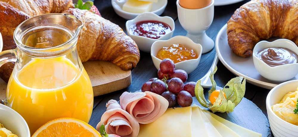 Ein Frühstücksbuffet mit Croissants, Obstsalat, Eiern, Käse und Kaffee auf einem Holztisch.