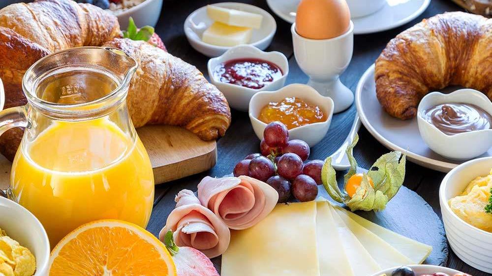 Ein Frühstücksbuffet mit Croissants, Obstsalat, Eiern, Käse und Kaffee auf einem Holztisch.