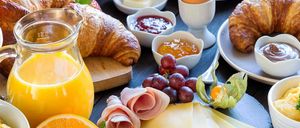 Ein Frühstücksbuffet mit Croissants, Obstsalat, Eiern, Käse und Kaffee auf einem Holztisch.