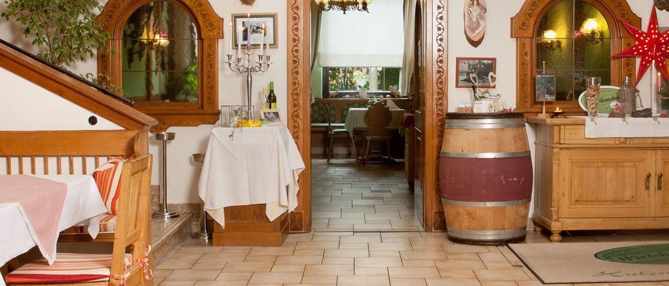 Das Innere eines Restaurants zeigt einen Holzfass, einen gefliesten Boden, Holzschränke und einen montierten Hirschkopf. Es gibt einen Kerzenständer mit Kerzen auf einem Tisch, der mit einem weißen Tuch bedeckt ist.