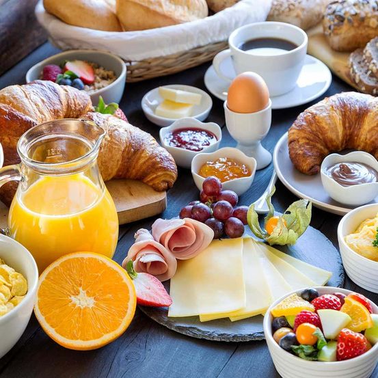 Ein Frühstückstisch mit Croissants, Eiern, Kaffee, Saft, Käse, Obst und Müsli.