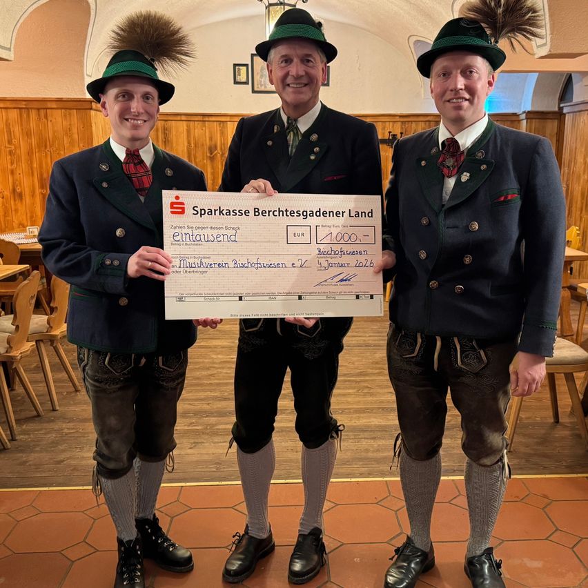 Drei Männer in traditioneller bayerischer Kleidung stehen zusammen und halten einen Scheck über 1000 Euro von der Sparkasse Berchtesgadener Land. Der Scheck ist auf den 4. Januar 2026 datiert.