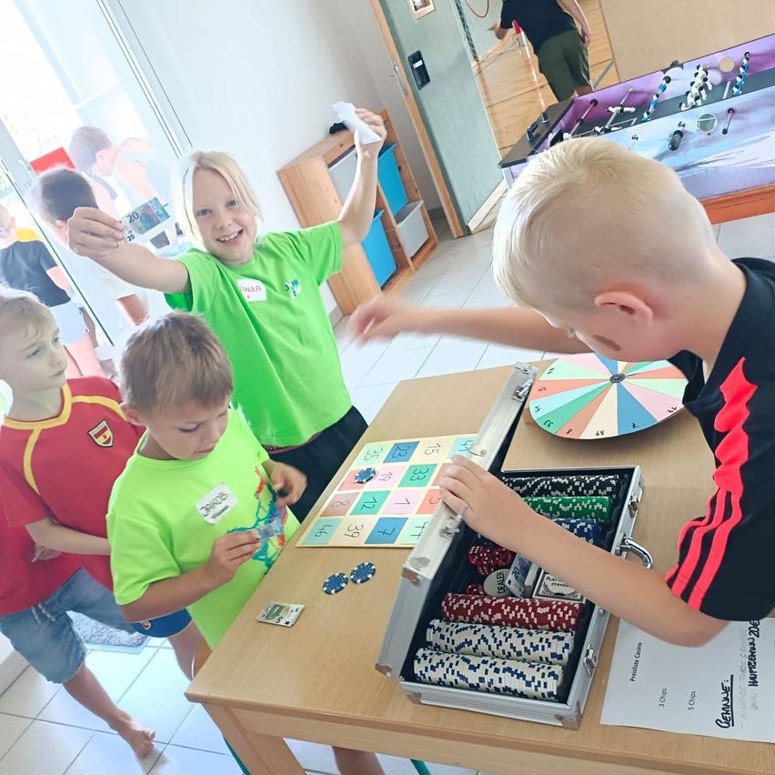 Mehrere Kinder spielen ein Spiel mit Pokerchips und einem Brettspiel auf einem Tisch in einem Raum.