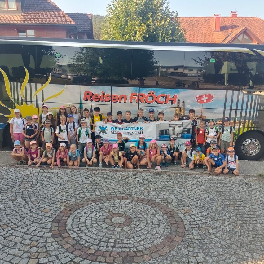 Eine Gruppe von Kindern und Erwachsenen posiert für ein Foto vor einem Bus mit einem Banner mit der Aufschrift Reisen Frosch.