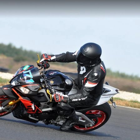 Ein Motorradfahrer fährt auf einer Straße ein schwarz-rotes Motorrad und trägt einen schwarzen Helm und einen Ledermantel mit der Nummer 9 auf dem Rücken.