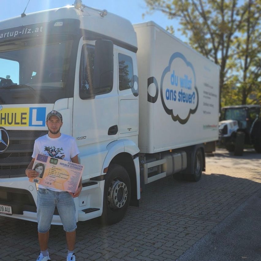 Ein Mann steht vor einem weissen Mercedes-Lkw, hält ein Zertifikat in der Hand und lächelt für die Kamera. Der Lkw hat gelbe Schrift auf der Vorderseite und eine blaue Sprechblase.