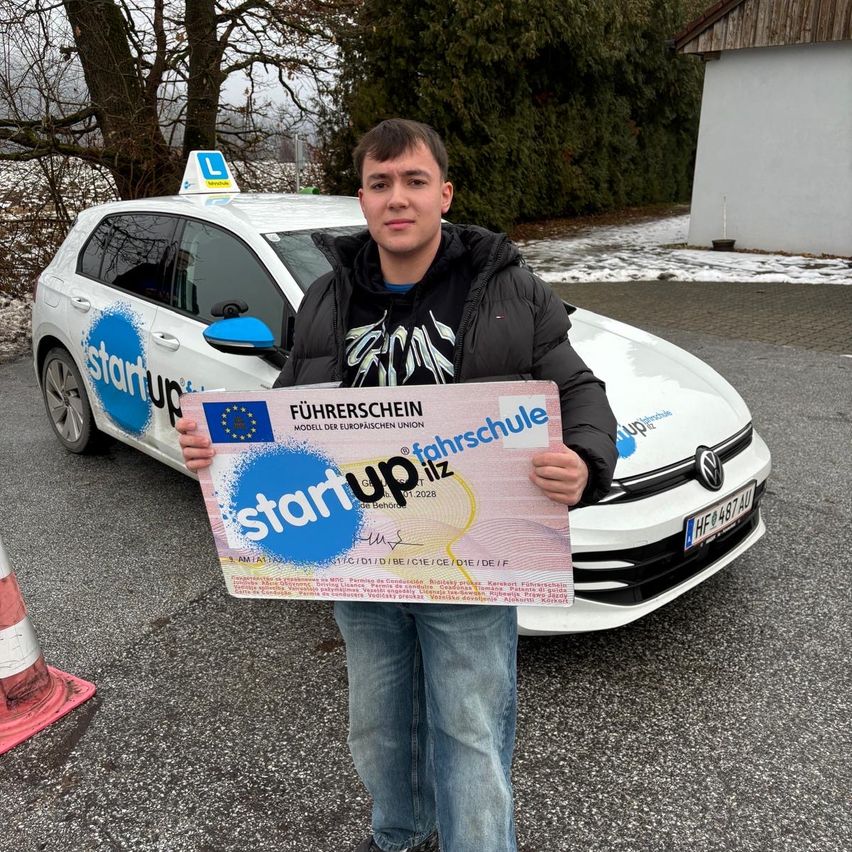 Ein Mann hält ein Zertifikat vor einem weißen Auto mit einem 'start up'-Schild und steht in einem verschneiten Bereich.