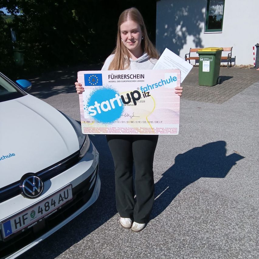 A girl holds a certificate labeled 'start up liz' in front of a white car with a license plate HF 484 AU.