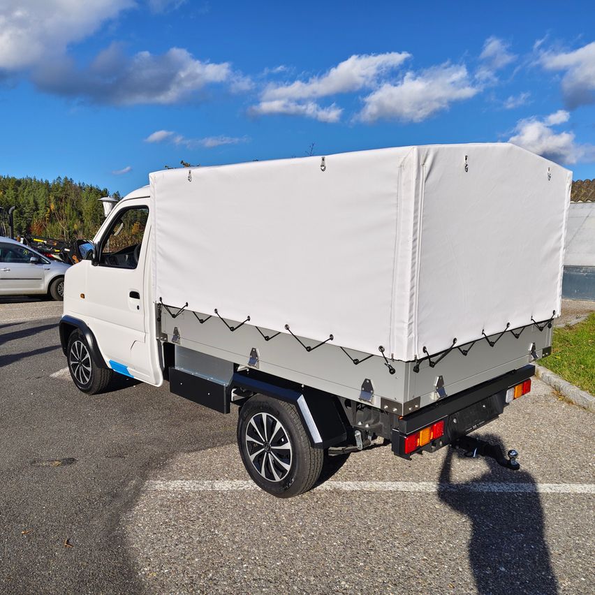 Ein weißer Lastwagen mit Abdeckung steht auf einem Parkplatz unter einem blauen Himmel mit verstreuten Wolken.